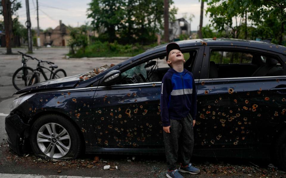 A child standing next to a damaged car looks up at a building destroyed during attacks in Irpin, on the outskirts Kyiv, Ukraine, Monday, May 30, 2022.  - AP Photo/Natacha Pisarenko