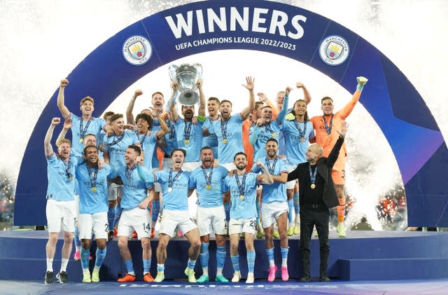 The Manchester City team celebrate winning the 2023 Champions League with the trophy on the presentation podium