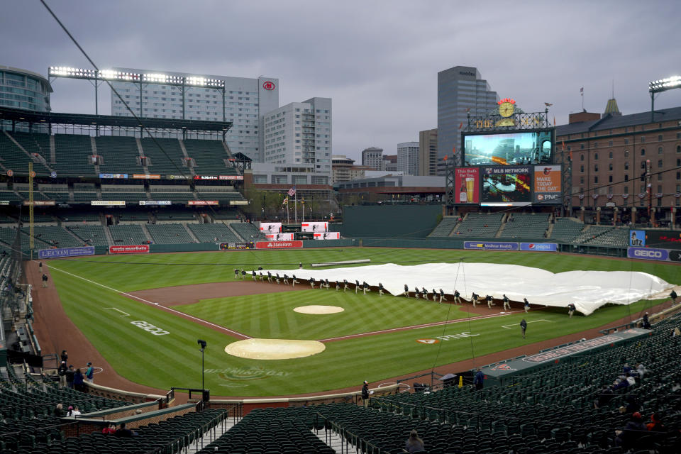 Grounds crew members place a tarp over the infield at Oriole Park at Camden Yards prior to a baseball game between the Baltimore Orioles and the Seattle Mariners, Monday, April 12, 2021, in Baltimore. (AP Photo/Julio Cortez)