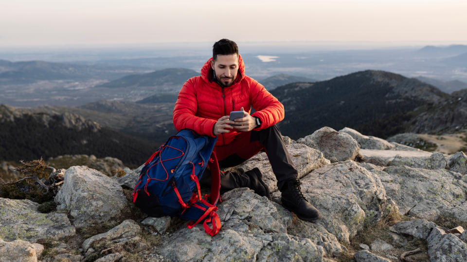 Man sitting on rocky mountain checking smartphone