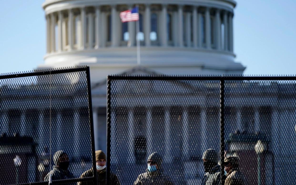 Members of the National Guard stand behind newly placed fencing around the Capitol grounds - AP