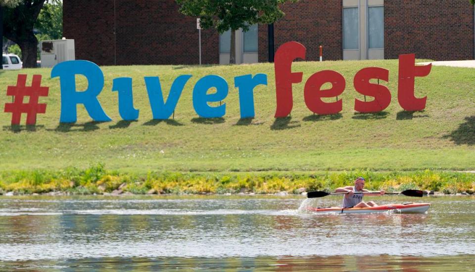 A kayaker paddles past a Riverfest sign along the Arkansas River.