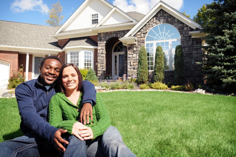 Color photo of a happy, young couple sitting in front of a new home.