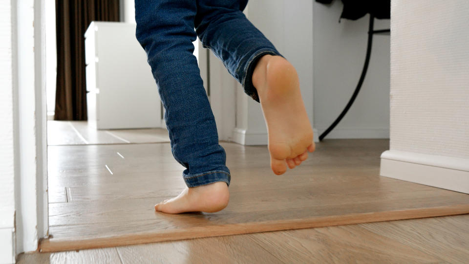 Child in jeans walking barefoot indoors, crossing from one room to another