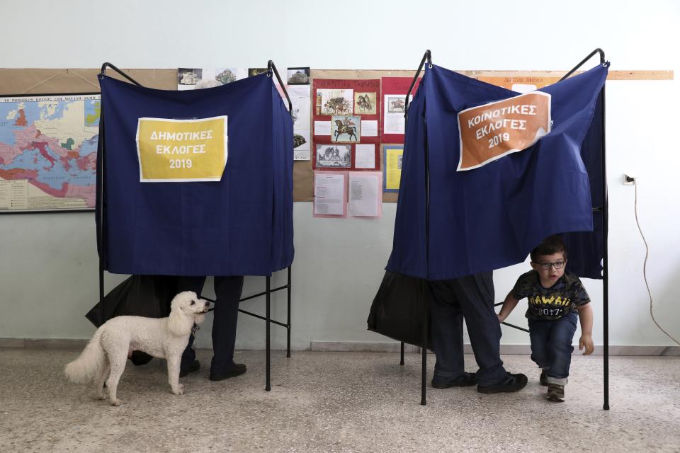 A boy looks out from a voting booth as a man holds his dog at a polling station in Athens on Sunday, May 26, 2019. Polls opened early Sunday in Greece, with nearly 10 million registered voters called upon to vote for the European Parliament, regional and local councils in 39,063 polling stations across the country. (AP Photo/Yorgos Karahalis)