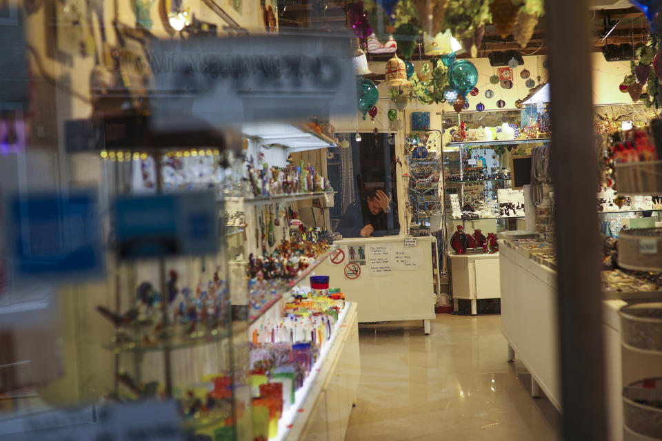 FILE - In this Monday, March 2, 2020 file photo, a shop assistant waits for customers at the Murano island in Venice, Italy. With the coronavirus emergency deepening in Europe, Italy, a focal point in the contagion, risks falling back into recession as foreign tourists are spooked from visiting its cultural treasures and the global market shrinks for prized artisanal products, from fashion to design. (AP Photo/Francisco Seco, File)