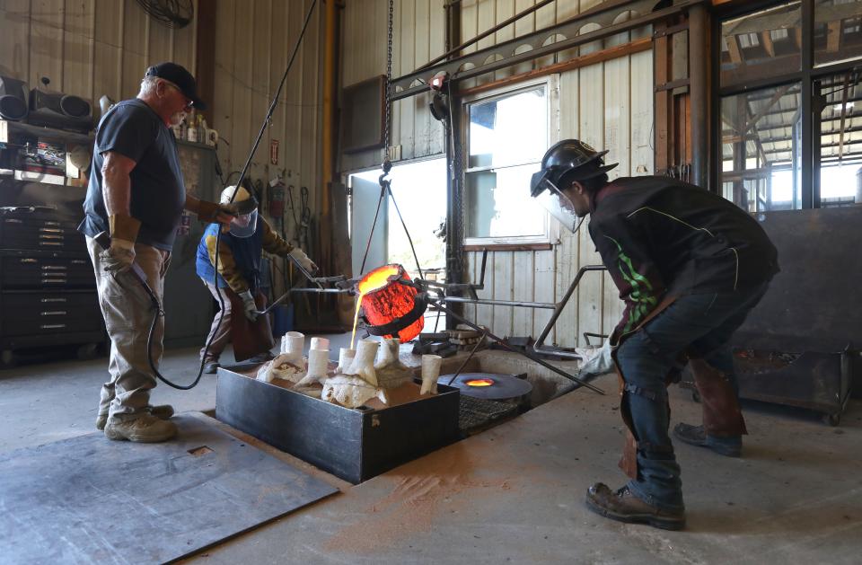 Charles Leasure, co-owner of Coopermill Bronze Works, mans the hoist while Jeff Becker, center, and Dan Minoski pour molten bronze into one of dozens of casts that will become a statue of Massillon football mascot Obie.