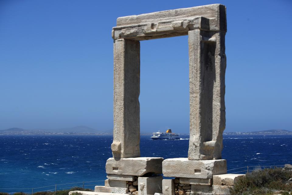 A ferry approaches the port as Portara, a marble gate which is part of an unfinished temple of Apollo of 530 B.C, stands atop of a hill on Aegean island of Naxos, Greece, Tuesday, May 11, 2021. (AP Photo/Thanassis Stavrakis)