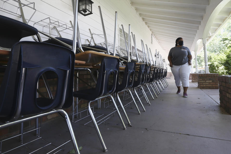 Teacher walks past a series of desks and chairs at school. 