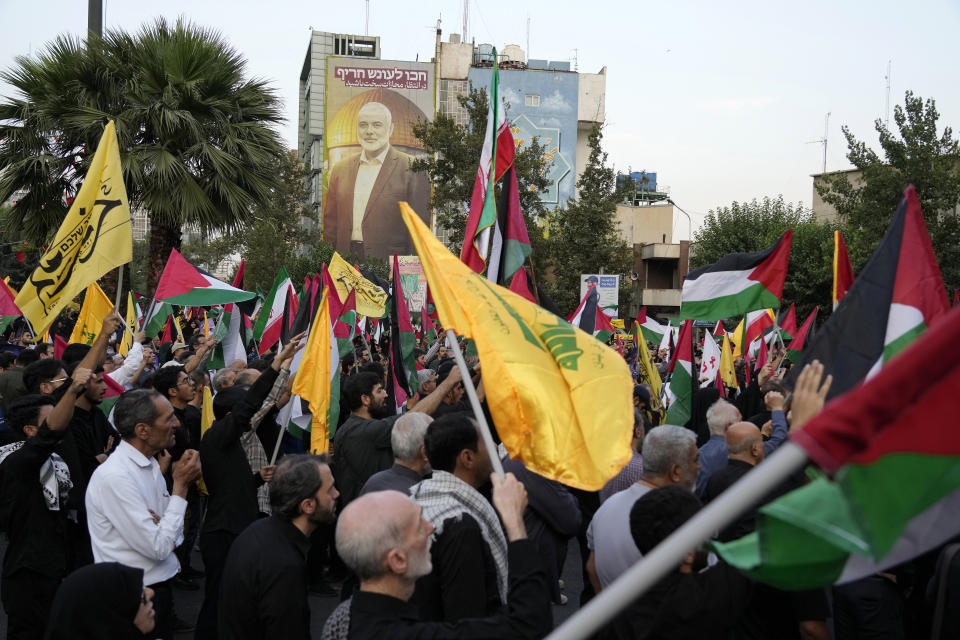 Iranian protesters wave Iranian, Palestinian and Lebanon's militant Hezbollah group flags in a demonstration to condemn the killing of Hamas leader Ismail Haniyeh as a huge portrait of him is seen on a wall at background, at Felestin (Palestine) Sq. in Tehran, Iran, Wednesday, July 31, 2024. Haniyeh was assassinated in Tehran, Iran's paramilitary Revolutionary Guard said early Wednesday. (AP Photo/Vahid Salemi)