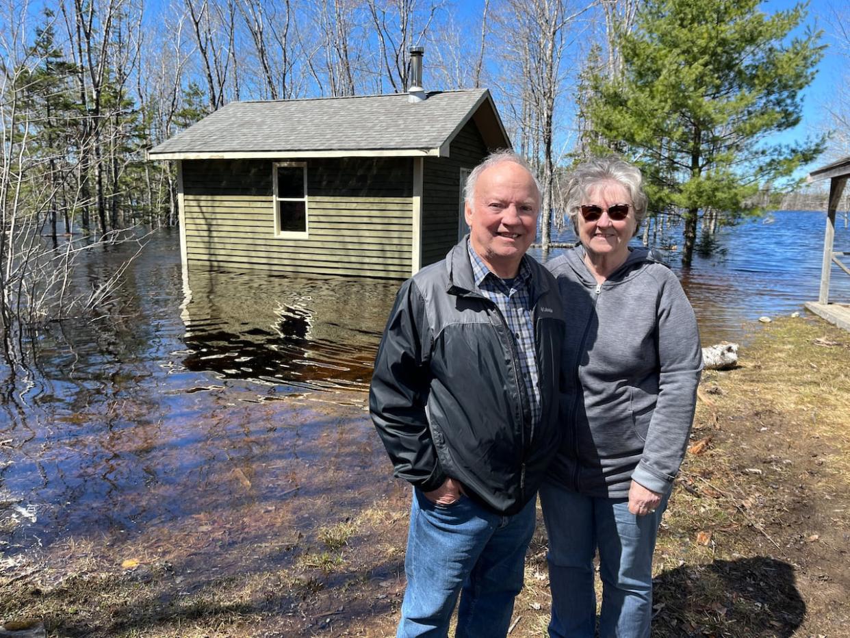 Doug and Carolyn Allen pose for a picture with their camp behind them in North Kemptville, Yarmouth County. The property has experienced flooding for years, but the water entered the camp for the first time this month. (Michael Gorman/CBC - image credit)