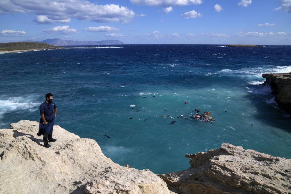 A local resident stands on a cliff as bodies of migrants are seen next floating debris after a sailboat carrying migrants smashed into rocks and sank off the island of Kythira, southern Greece, Thursday, Oct. 6, 2022. Residents of a Greek island pulled shipwrecked migrants to safety up steep cliffs in dramatic rescues after two boats sank in Greek waters, leaving at least 21 people dead and many still missing. (AP Photo/Thanassis Stavrakis)