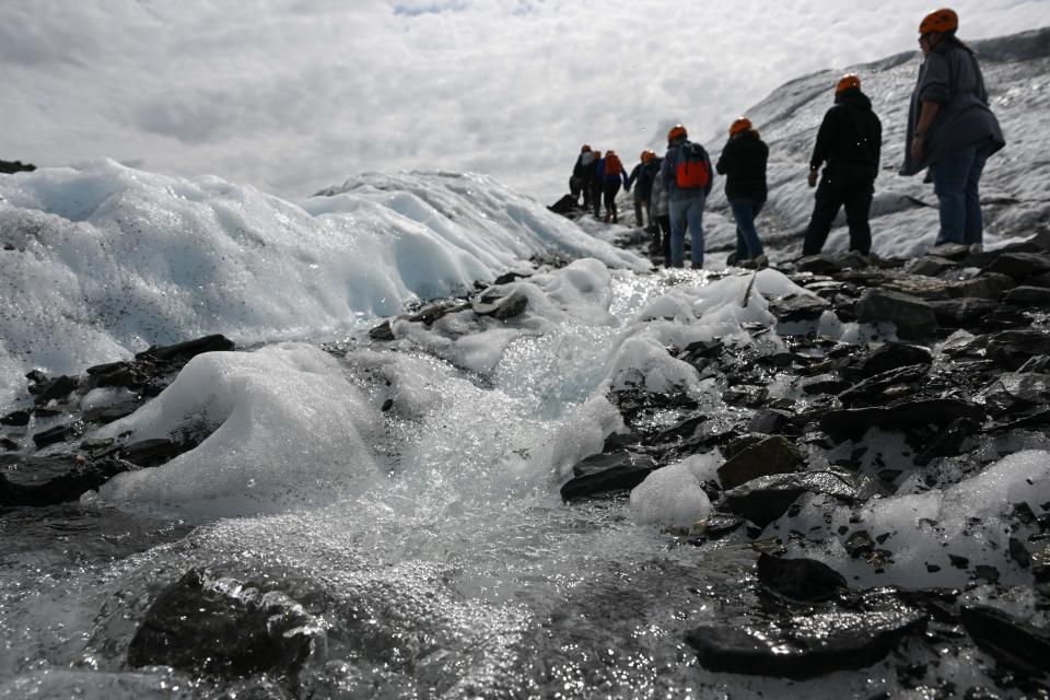 Warmly clad visitors in single file pick their way through a melting glacier.