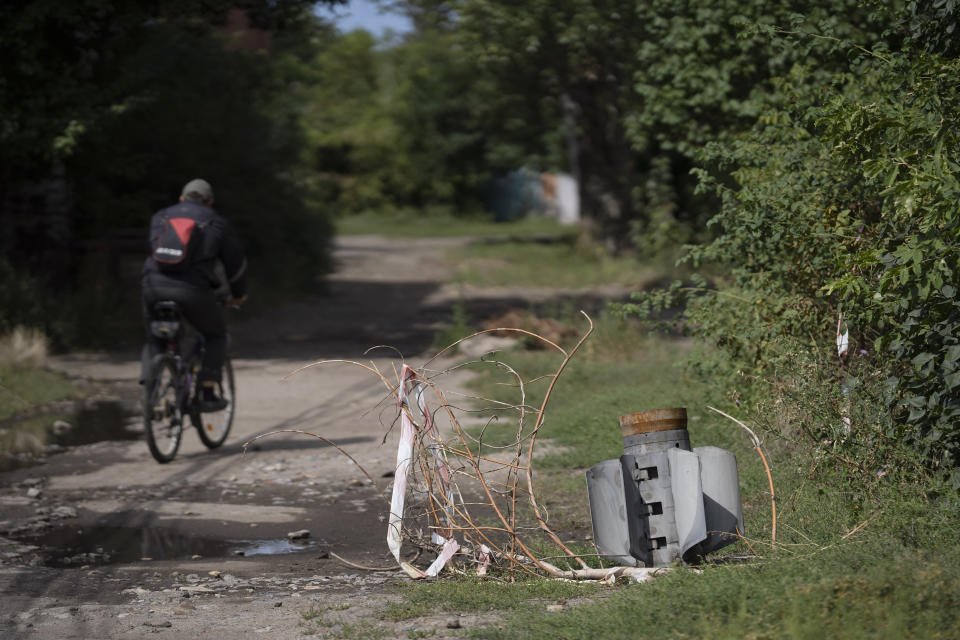 A man cycles past part of a rocket that sits wedged in the ground at a residential area in Sloviansk, Ukraine, Monday, Sept. 5, 2022. (AP Photo/Leo Correa)