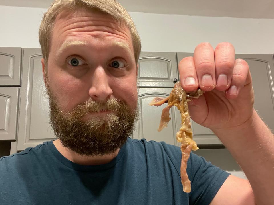 The writer makes a disappointed face and holds of a piece of Walmart rotisserie-chicken skin