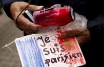 A man holds a candle and a drawing depicting the French flag and carrying the words "I am Parisian" in front of the French embassy after attacks in Paris on Friday, in Warsaw, Poland November 14, 2015. REUTERS/Kacper Pempel