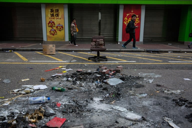 People walk past burnt debris scattered across the street following overnight clashes between protesters and police in the Mongkok area of Hong Kong on February 9, 2016