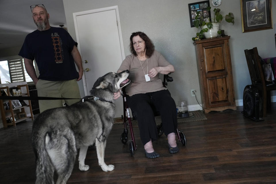 Maria Jackson, right, meets the dog of her new roommate as she moves into a room at a home with the help of friend David Mcfarlan, left, Monday, May 8, 2023, in Las Vegas. Jackson, a longtime massage therapist, lost her customers when the pandemic triggered a statewide shutdown in March 2020 and was evicted from her apartment earlier this year. (AP Photo/John Locher)