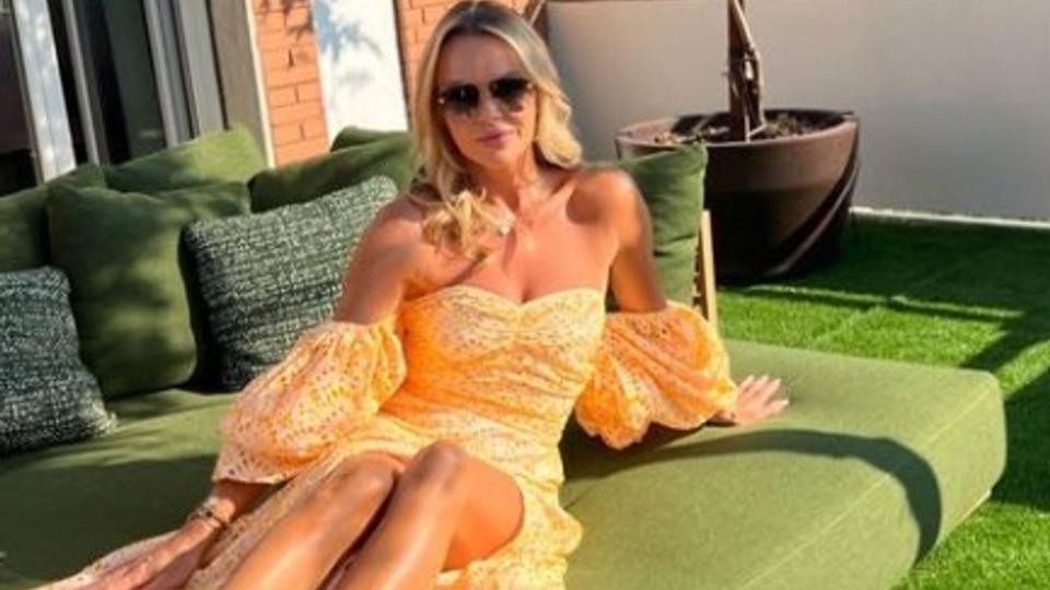 Amanda Holden wearing orange off the shoulder dress posing on green outdoor sofa