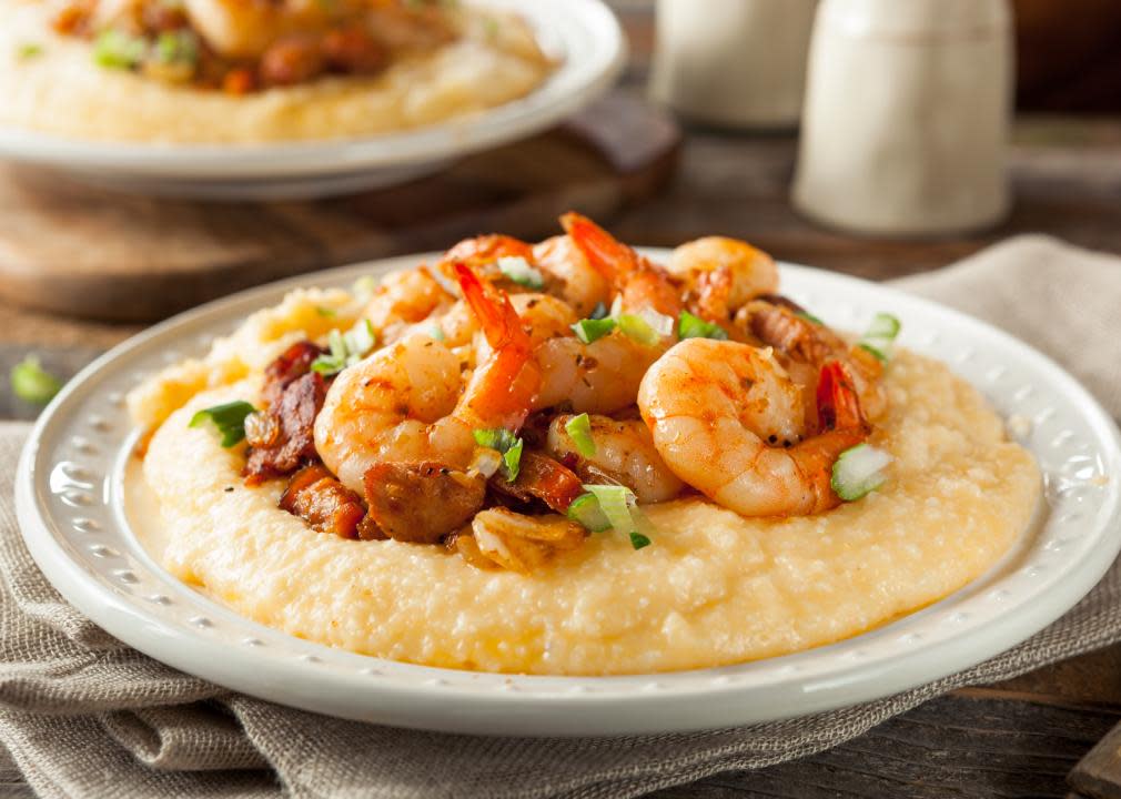 A bowl of shrimp and grits on a table with another bowl in the background. 