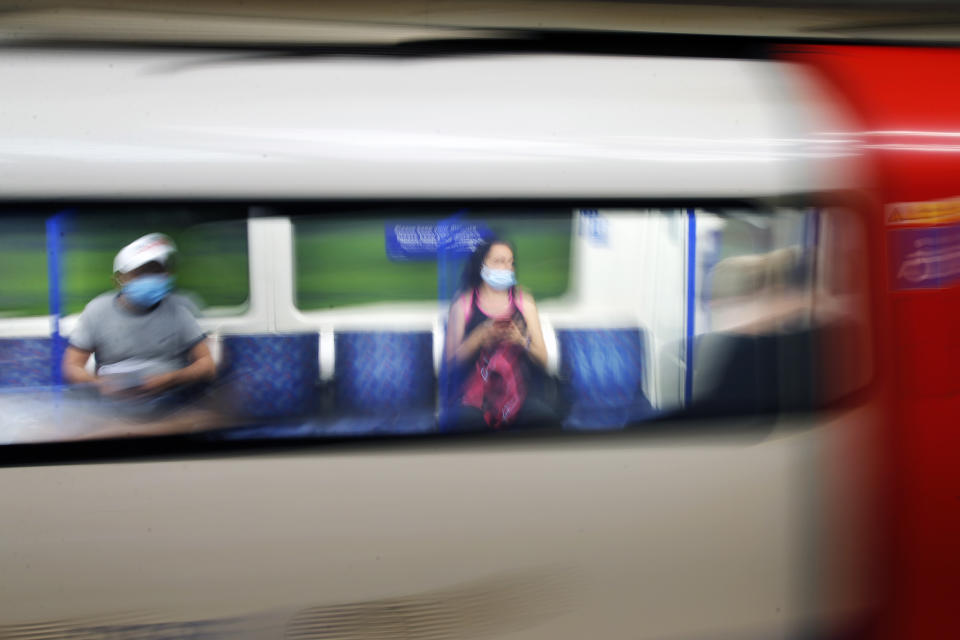 Two people wearing protective masks sit two seats apart on a moving London underground train as the UK continues to recover from the coronavirus pandemic.