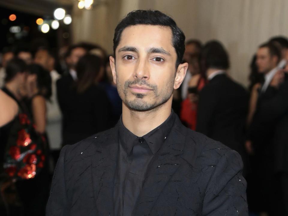 Riz Ahmed, wearing all black, poses at an event.