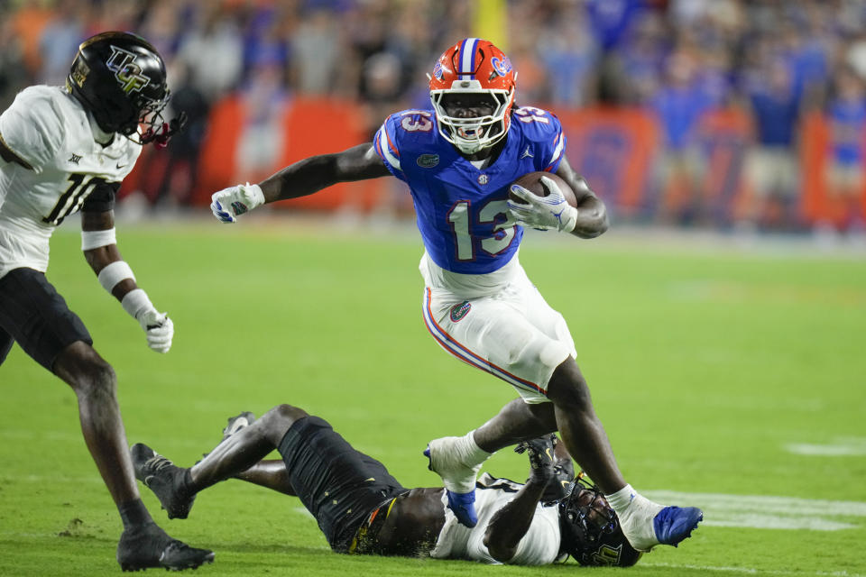 Florida running back Jadan Baugh (13) breaks a tackle as he gets by Central Florida defensive back Ladarius Tennison, bottom, and defensive back Brandon Adams, left, for yardage during the first half of an NCAA college football game, Saturday, Oct. 5, 2024, in Gainesville, Fla. (AP Photo/John Raoux)