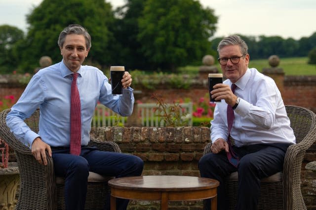 Taoiseach Simon Harris and Sir Keir Starmer each raise a glass of Guinness  while sitting down at a table in the garden at Chequers