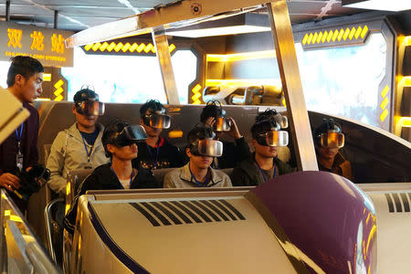 Staff members wearing virtual reality (VR) goggles sit in a motorized cart while performing an inspection of the attraction "Fly Over Guizhou", at the Oriental Science Fiction Valley theme park in Guiyang, Guizhou province, China November 16, 2017. REUTERS/Joseph Campbell/Files