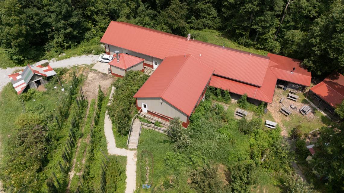 An aerial photo of Scratch Brewing Co. shows rows of trellises with growing hops, tables in a small courtyard, and many acres of woods stretching on behind the establishment.