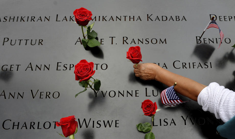 FILE - In this Sept. 11, 2014, file photo, a woman places flowers in the inscribed names along the edge of the North Pool during memorial observances on the 13th anniversary of the Sept. 11, 2001 terror attacks on the World Trade Center in New York. The coronavirus pandemic has reshaped how the U.S. is observing the anniversary of 9/11. The terror attacks' 19th anniversary will be marked Friday, Sept. 11, 2020, by dueling ceremonies at the Sept. 11 memorial plaza and a corner nearby in New York. (AP Photo/Justin Lane, Pool, File)