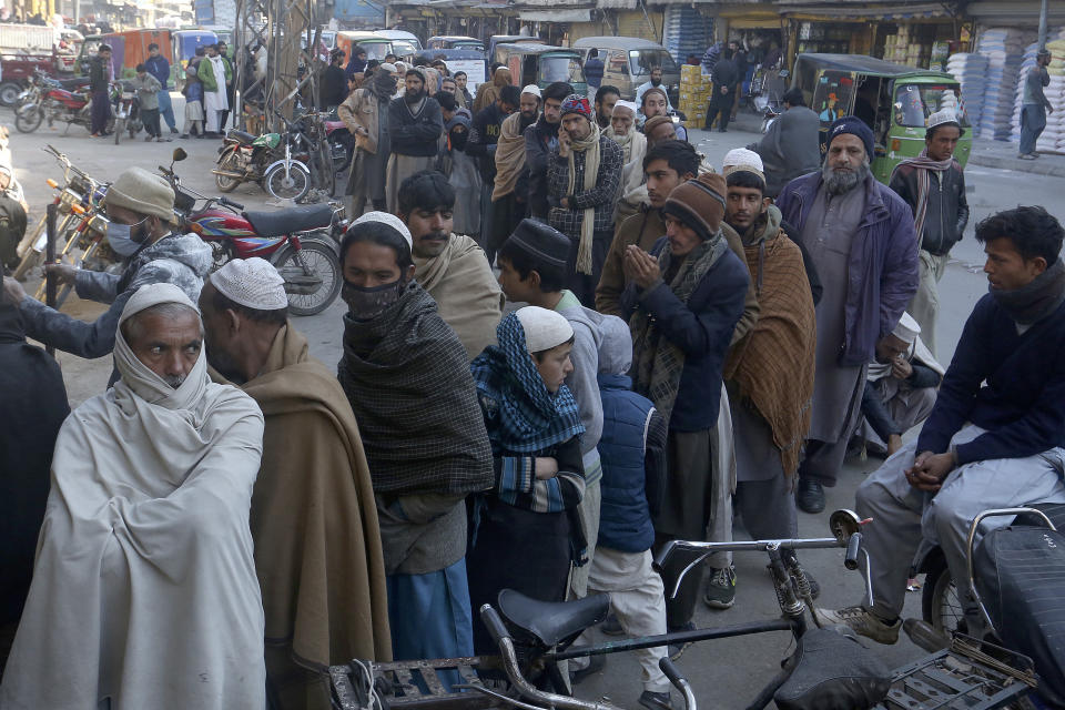 People stand in a long queue and wait to buy subsidized sacks of wheat-flour from a sale point in Peshawar, Pakistan, Monday, Jan. 9, 2023. People are suffering from recent price hike in wheat-flour in Pakistan. (AP Photo/Muhammad Sajjad)