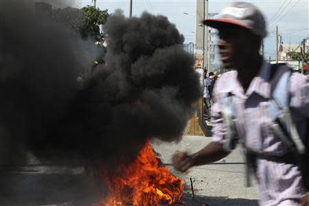 A man runs near a burning tyre during protests in Port-au-Prince November 18, 2013. REUTERS/Marie Arago