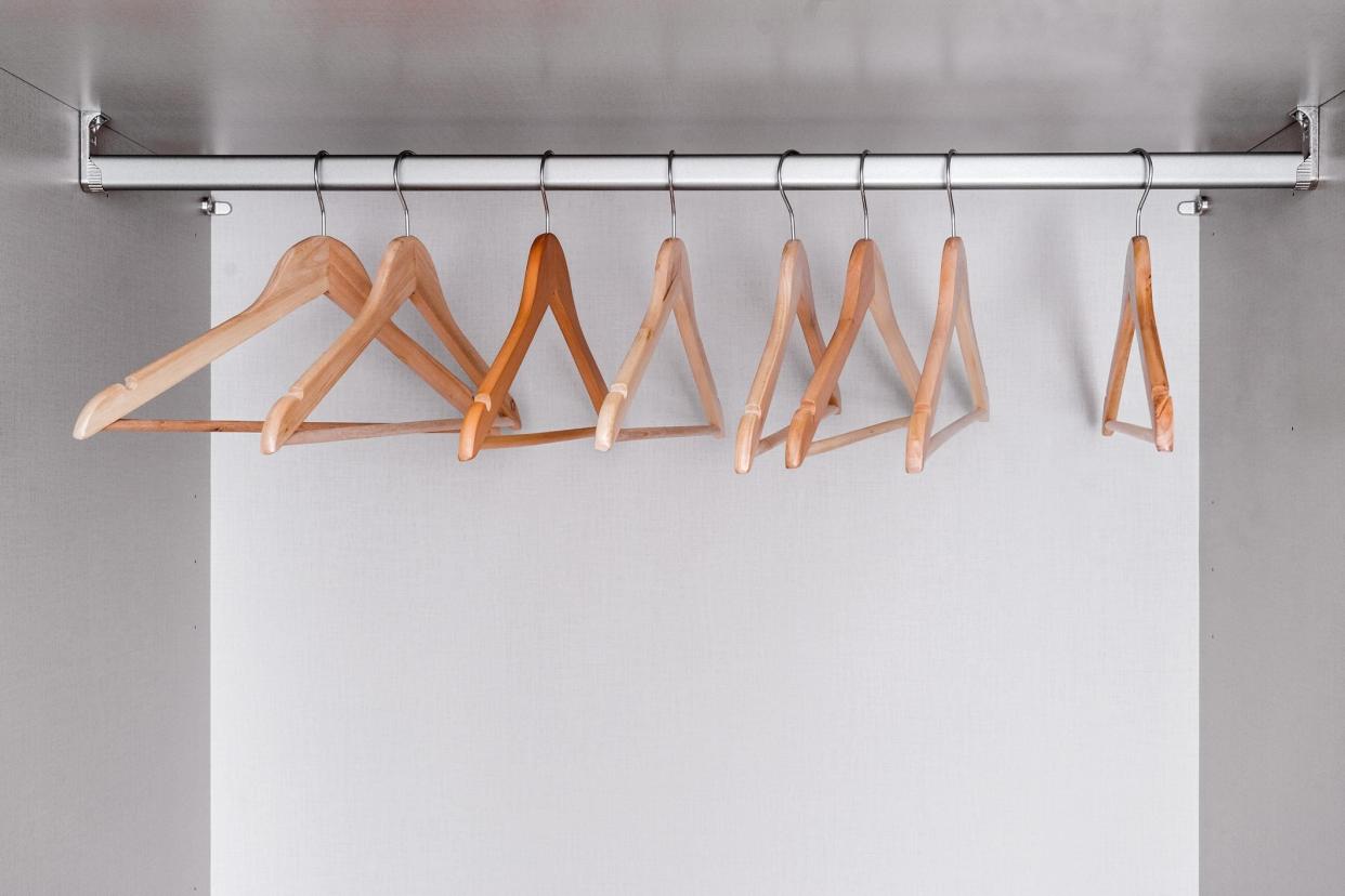 Many empty, lacquered light wood clothes hangers hang in wardrobe on metal rod. Internal space of furniture