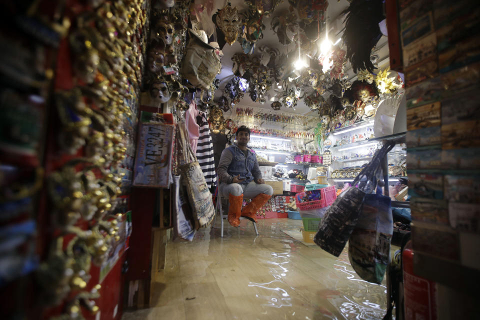 A mask seller sits on a chair in his shop as water floods the premises (AP