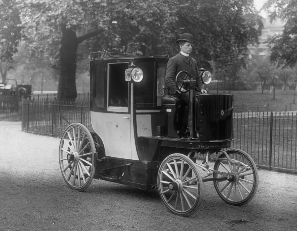 A historical photograph of a man driving a 1896 Bersey Electric cab.