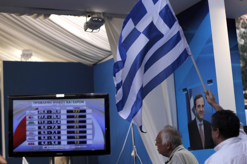 New Democracy conservative party supporters wave a Greek flag as a TV screen shows results at an election kiosk at Syntagma square in Athens, Sunday, June 17, 2012. The pro-bailout New Democracy party came in first Sunday in Greece's national election, and its leader has proposed forming a pro-euro coalition government.(AP Photo/Petros Giannakouris)