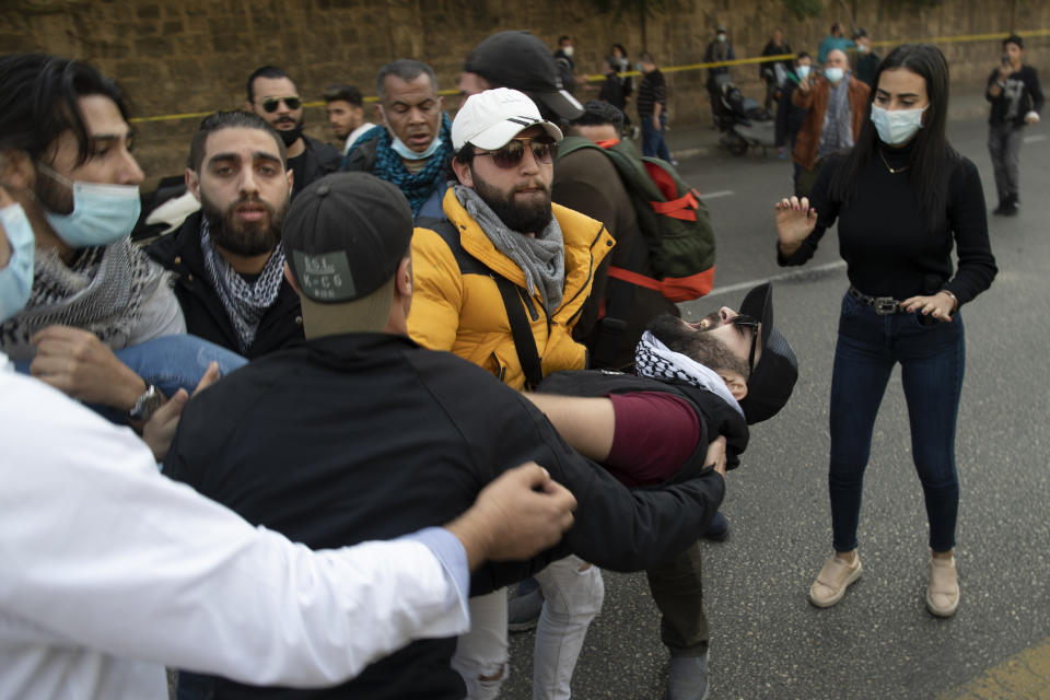 Protestors hold an injured man during a scuffle between riot police and anti-government protesters outside a military court, in Beirut, Lebanon, Monday, Feb. 8, 2021. Riot police briefly clashed Monday in Beirut with hundreds of protesters demanding the release of anti-government activists detained following riots in northern Lebanon late last month. (AP Photo/Hassan Ammar)