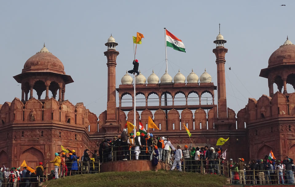 FILE - In this Tuesday, Jan. 26, 2021, file photo, a Sikh man hangs on to pole holding a Sikh religious flag along with a farm union flag at the historic Red Fort monument during a farmers protest against new farm laws in New Delhi, India. A sea of tens of thousands of farmers riding tractors and horses stormed India’s historic Red Fort this week — a dramatic escalation of their protests, which are posing a major challenge to Prime Minister Narendra Modi’s government. (AP Photo/Dinesh Joshi, File)