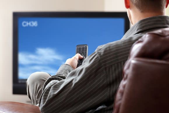 A man presses a remote at his television in a living room.