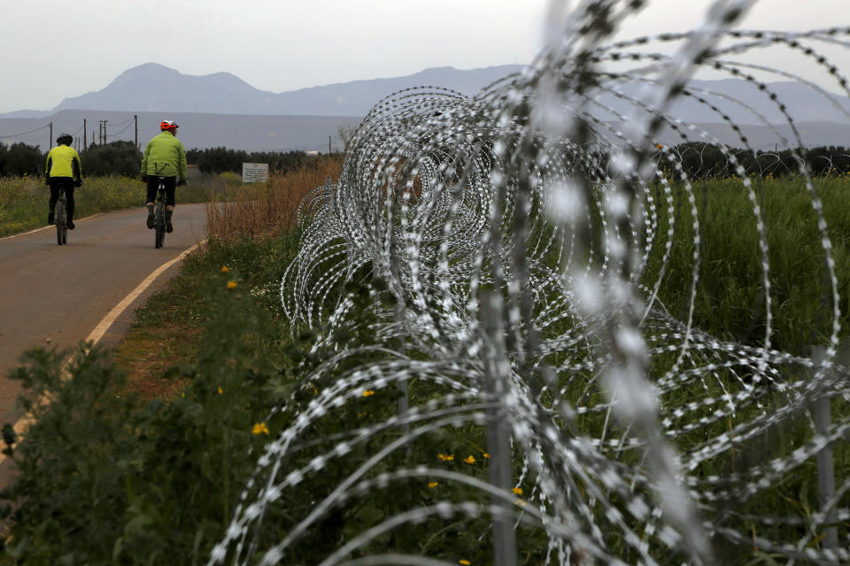 Two men cylce along a row of razor wire along the southern side of a U.N buffer zone that cuts across the ethnically divided Cyprus, during sunset near village of Astromeritis, Tuesday, March 9, 2021. The government of ethnically split Cyprus has come under fire over a decision to lay razor wire along a section of a U.N. controlled buffer zone it said is needed to stem migrant inflows from the island's breakaway north, with critics charging that the "ineffective" scheme only feeds partitionist perceptions amid a renewed push resume dormant peace talks. (AP Photo/Petros Karadjias)