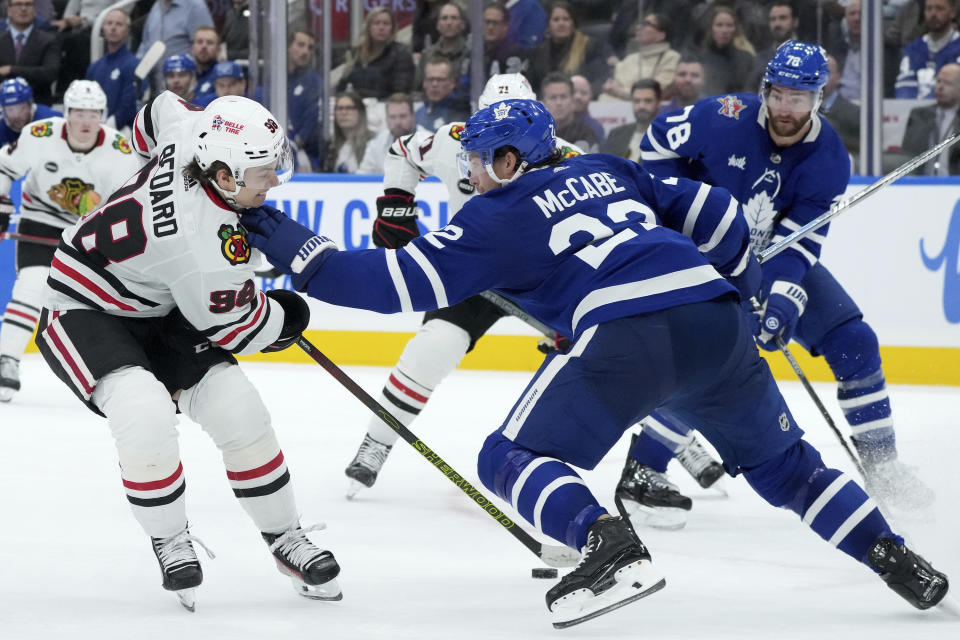 Chicago Blackhawks center Connor Bedard (98) tries to get past Toronto Maple Leafs defenseman Jake McCabe (22) during third-period NHL hockey game action in Toronto, Monday, Oct. 16, 2023. (Nathan Denette/The Canadian Press via AP)