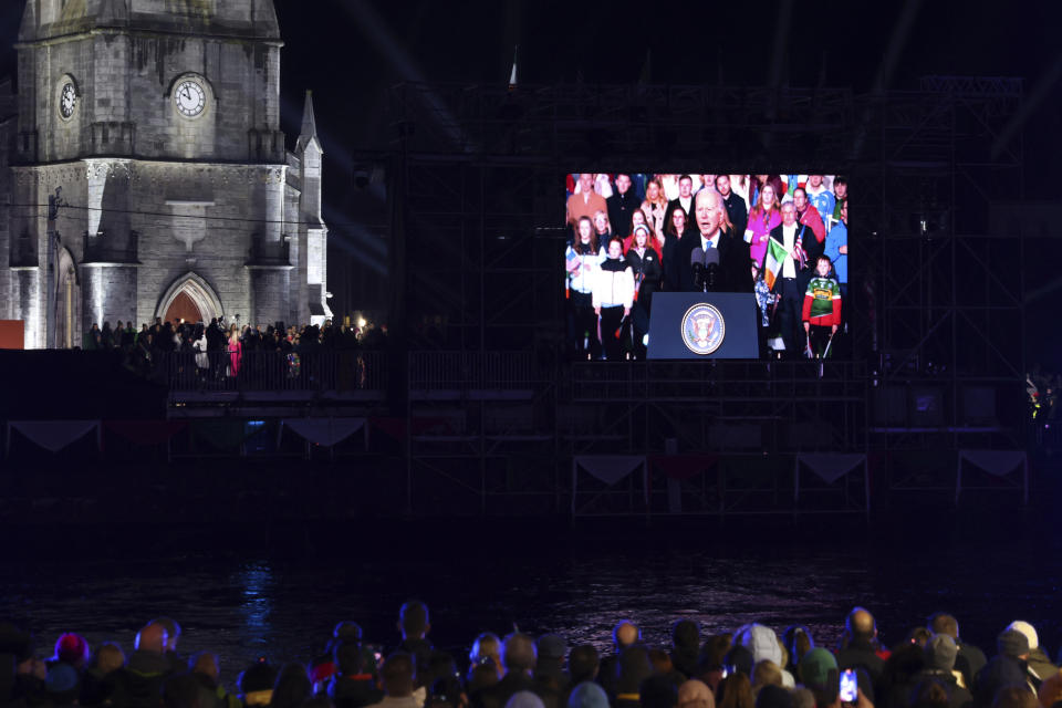 People watch a large screen showing President Joe Biden speaking outside St. Muredach's Cathedral in Ballina, Ireland, Friday, April 14, 2023. (AP Photo/Peter Morrison)