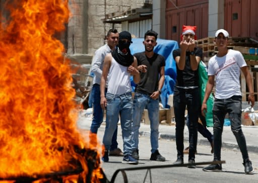 Stone-carrying Palestinians near Hebron stand behind a burning tyre as they protest against a US-led Middle East conference in Bahrain