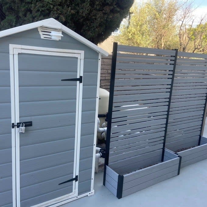 A plastic shed next to a wooden slat fence with a built-in planter, situated in an outdoor area