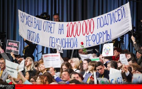 Journalists wave posters and a banner about a controversial hike in the pension age in hopes of grabbing Mr Putin's attention - Credit: Sergei Bobylev/TASS via Getty