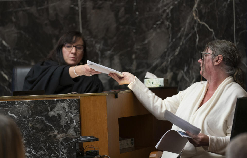 Judge Cheryl Matthews, left, hands Jennifer Crumbley photos that were entered into evidence as Crumbley's attorney Shannon Smith questions her as Crumbley testifies during her trial, Thursday, Feb. 1, 2024, in Pontiac, Mich. Crumbley, 45, is charged with involuntary manslaughter. Prosecutors say she and her husband were grossly negligent and could have prevented the four deaths if they had tended to their son’s mental health. They’re also accused of making a gun accessible at home. (Mandi Wright/Detroit Free Press via AP, Pool)