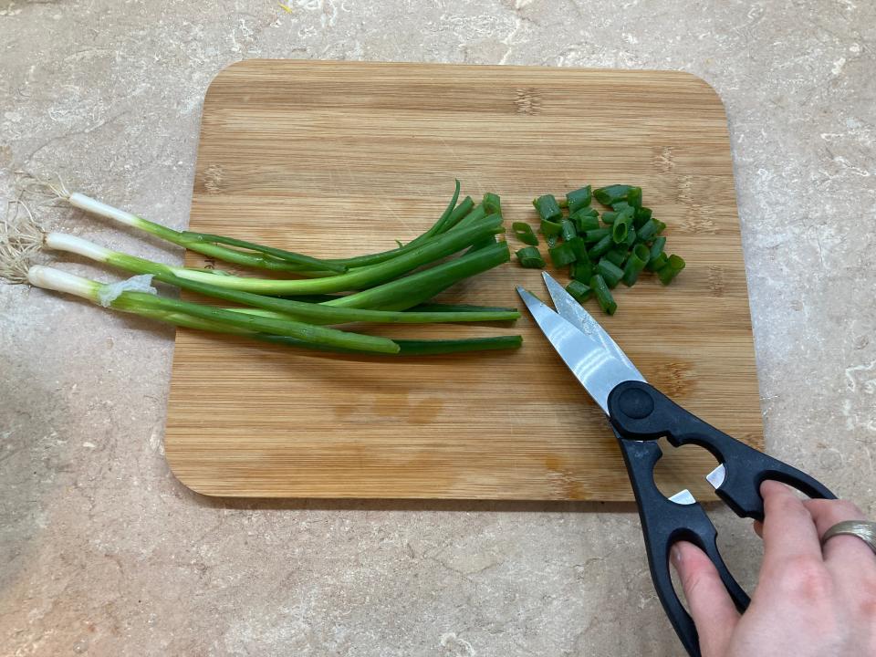 Cutting green onions with kitchen shears on a countertop.