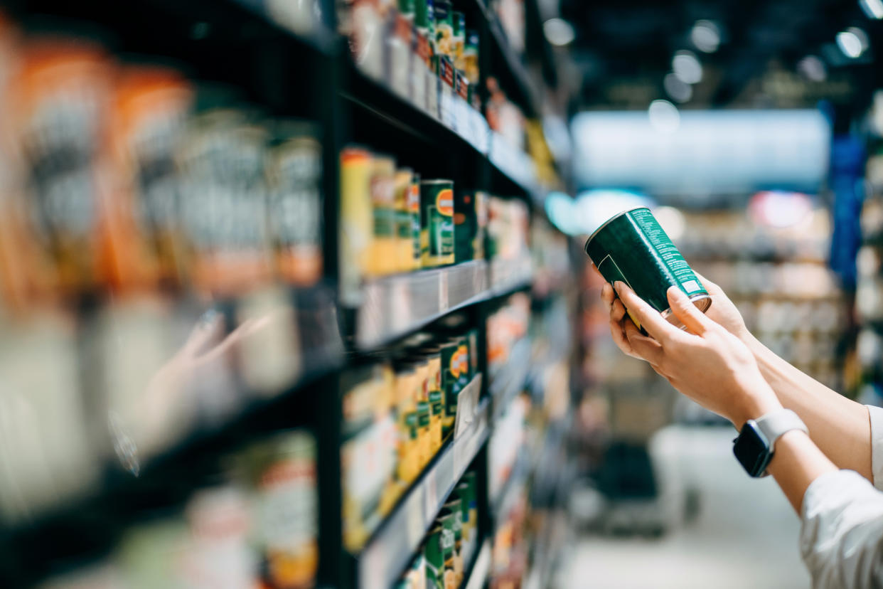 Canned foods. Close up of a woman grocery shopping in supermarket. Holding a tin can and reading the nutrition label at the back