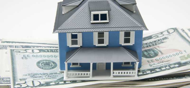 A blue model home sitting on stacks of cash.